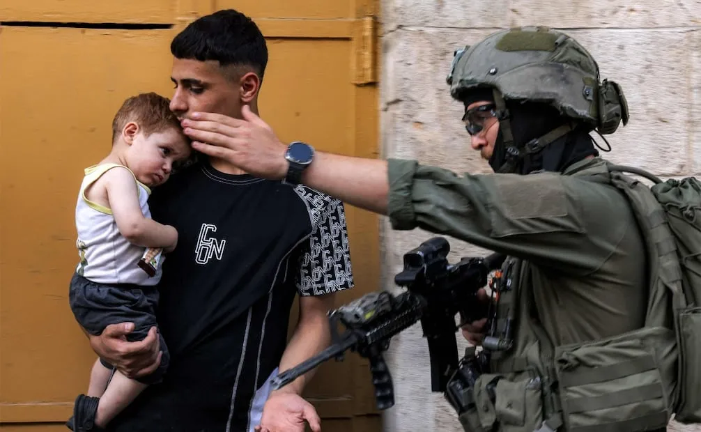 Un soldado israelí indica a un hombre que carga a un menor que abandone el mercado del casco antiguo de Hebrón mientras se desarrolla la evacuación de palestinos durante la visita de colonos israelíes (25/07/2026). Foto: AFP